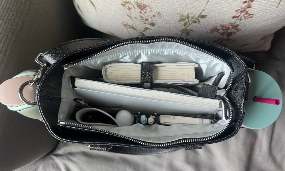 black carina tote bag by white elm packed with book, planner, sunglasses, pens and water bottles