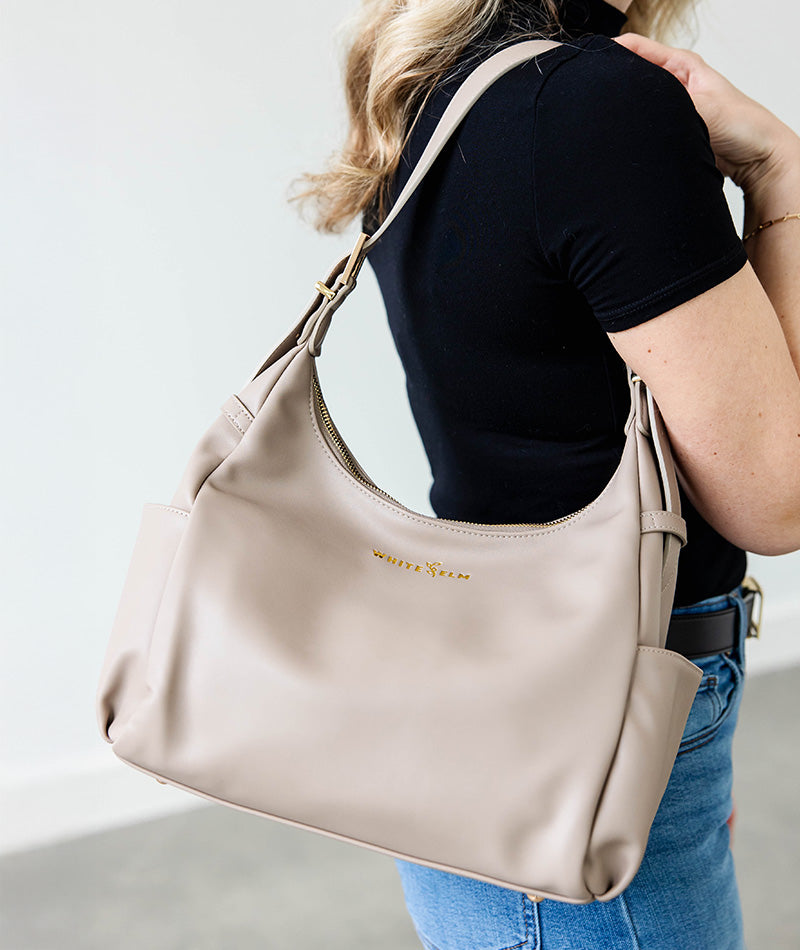 Person wearing a taupe camille handbag with 'White Elm' branding on a plain background