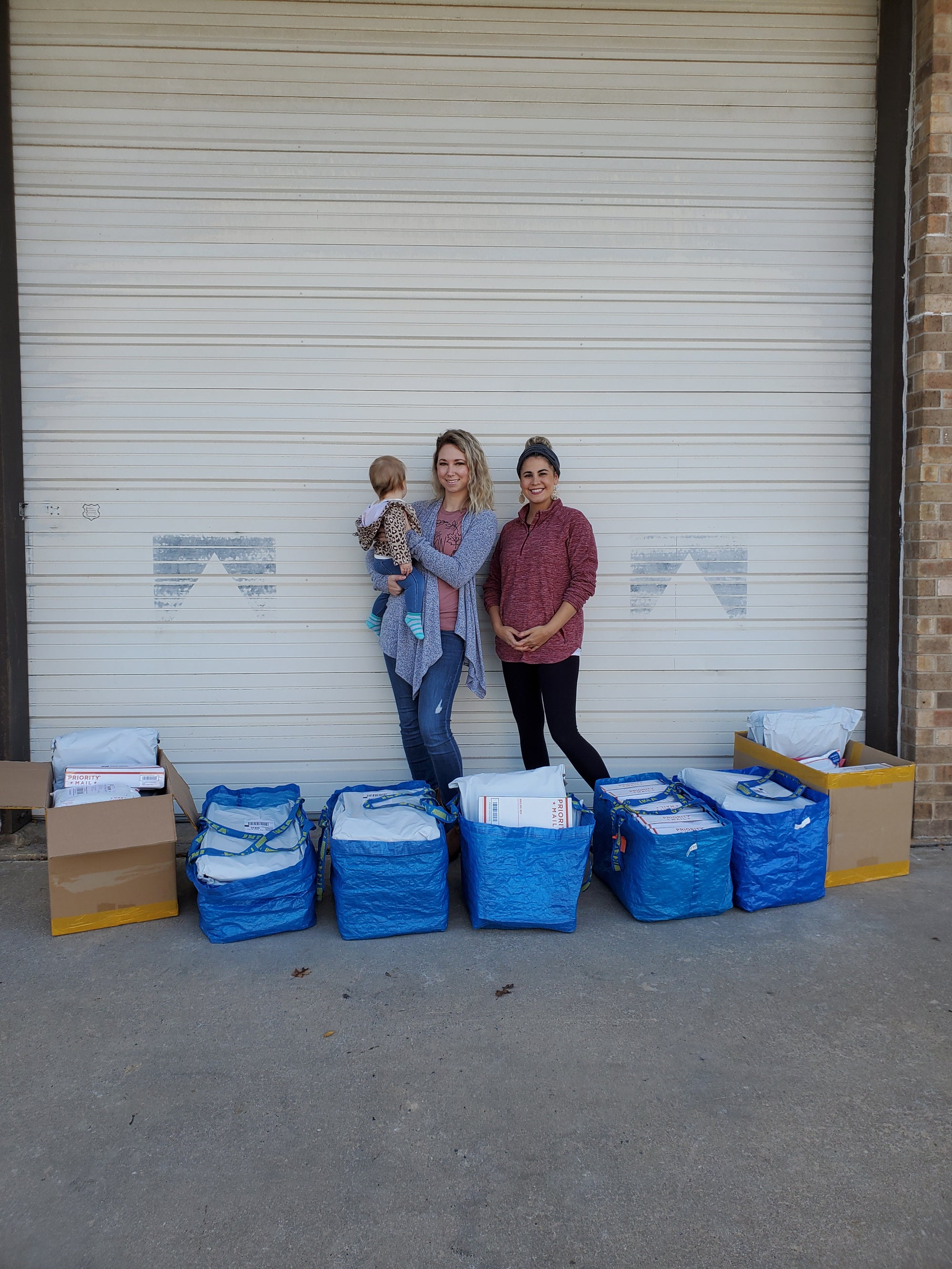 Three people standing in front of a white metal garage door with several blue and white storage bags and cardboard boxes beside them.