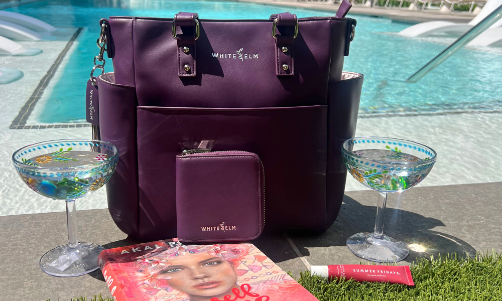 Purple handbag and wallet with 'White Elm' branding by a poolside.