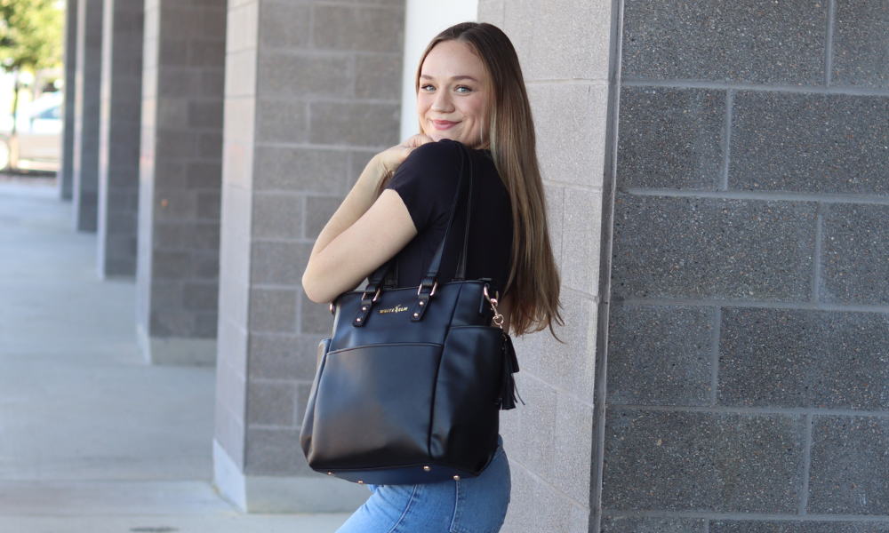 Woman holding a black handbag against a gray stone wall.