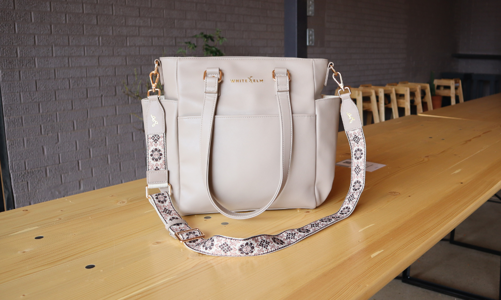 taupe carina tote back with decorative statement strap by white elm sitting on wood table