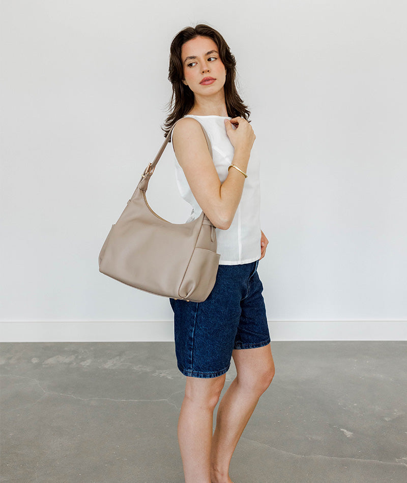 Woman holding a taupe handbag against a plain background