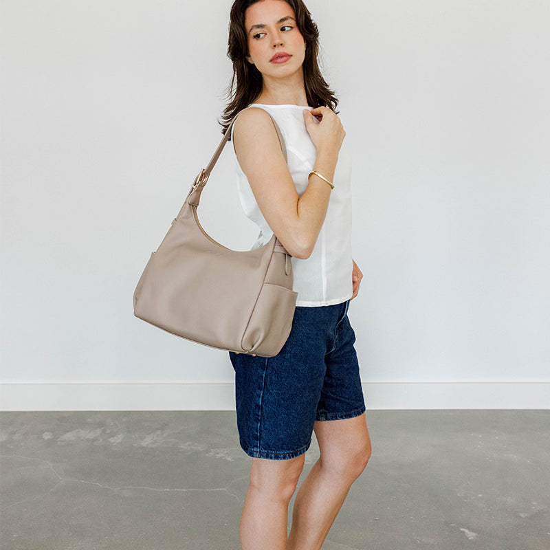 Woman holding a taupe handbag against a plain background