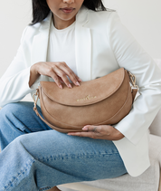 Woman holding the Almond Emily Crescent bag by its strap