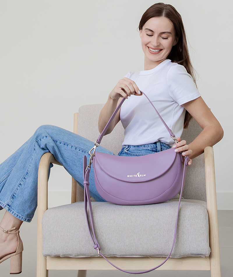 Woman holding the Heather Purple Emily Crescent bag by its strap