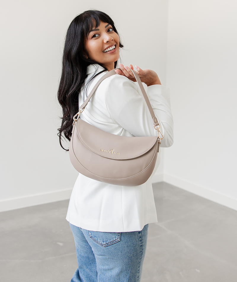 Woman holding the Taupe Emily Crescent bag by its strap