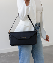 Woman carrying the black Noemi east west bag on her forearm in a white blazer