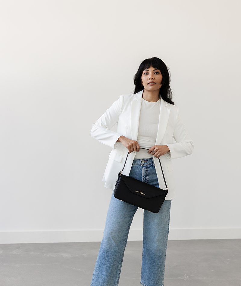 Black Noemi shoulder bag held by the strap at waist height