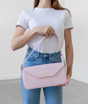 Blush pink Noemi shoulder bag held by the strap in front of the body