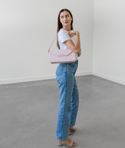 Woman wearing the blush pink Noemi east west bag, looking back over her shoulder