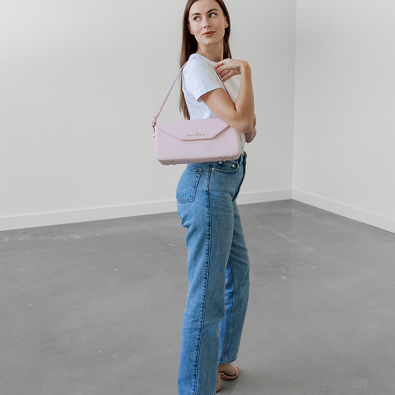 Woman wearing the blush pink Noemi east west bag, looking back over her shoulder