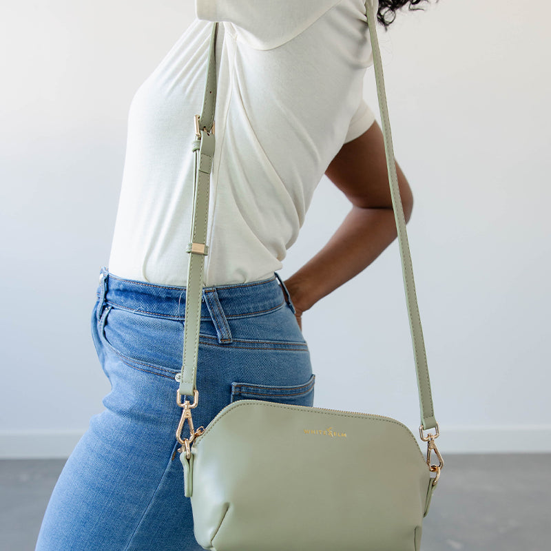 Person wearing a light green handbag with a strap over the shoulder against a neutral background