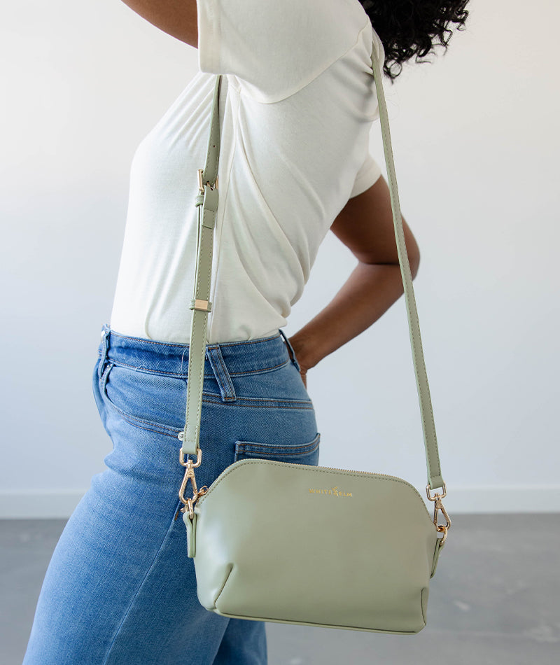 Person wearing a light green handbag with a strap over the shoulder against a neutral background
