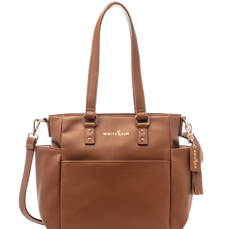 A caramel-colored tote bag made from vegan leather with gold hardware, featuring a structured design with a top zipper, and carrying handles.