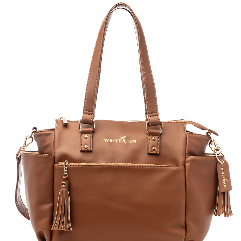 A caramel-colored Gemini Mini Convertible Backpack with multiple compartments and tassel detail, designed for versatile carrying options.