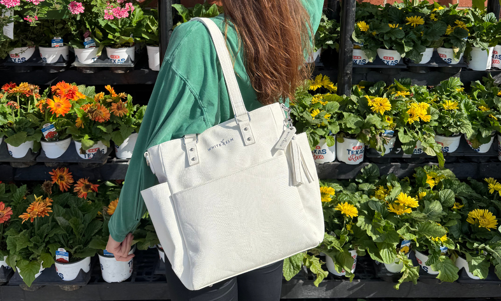Person holding a white tote bag in front of flower plants